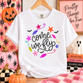 White Comfort Colors tee with come, we fly lettering, colorful broomsticks and stars, and black bats