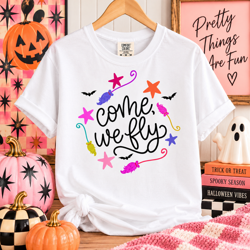 White Comfort Colors tee with come, we fly lettering, colorful broomsticks and stars, and black bats