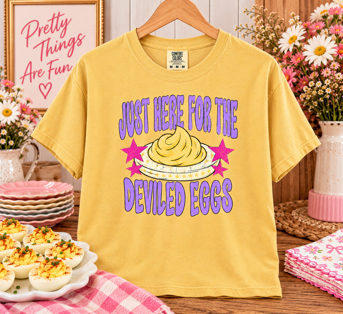 Mustard Comfort Colors tee with purple Just Here for the Deviled Eggs lettering, pink stars, and a deviled egg illustration